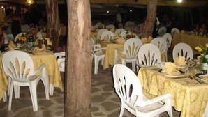 Un área de comedor al aire libre con mesas redondas cubiertas con manteles amarillos, rodeada de sillas de plástico blanco.