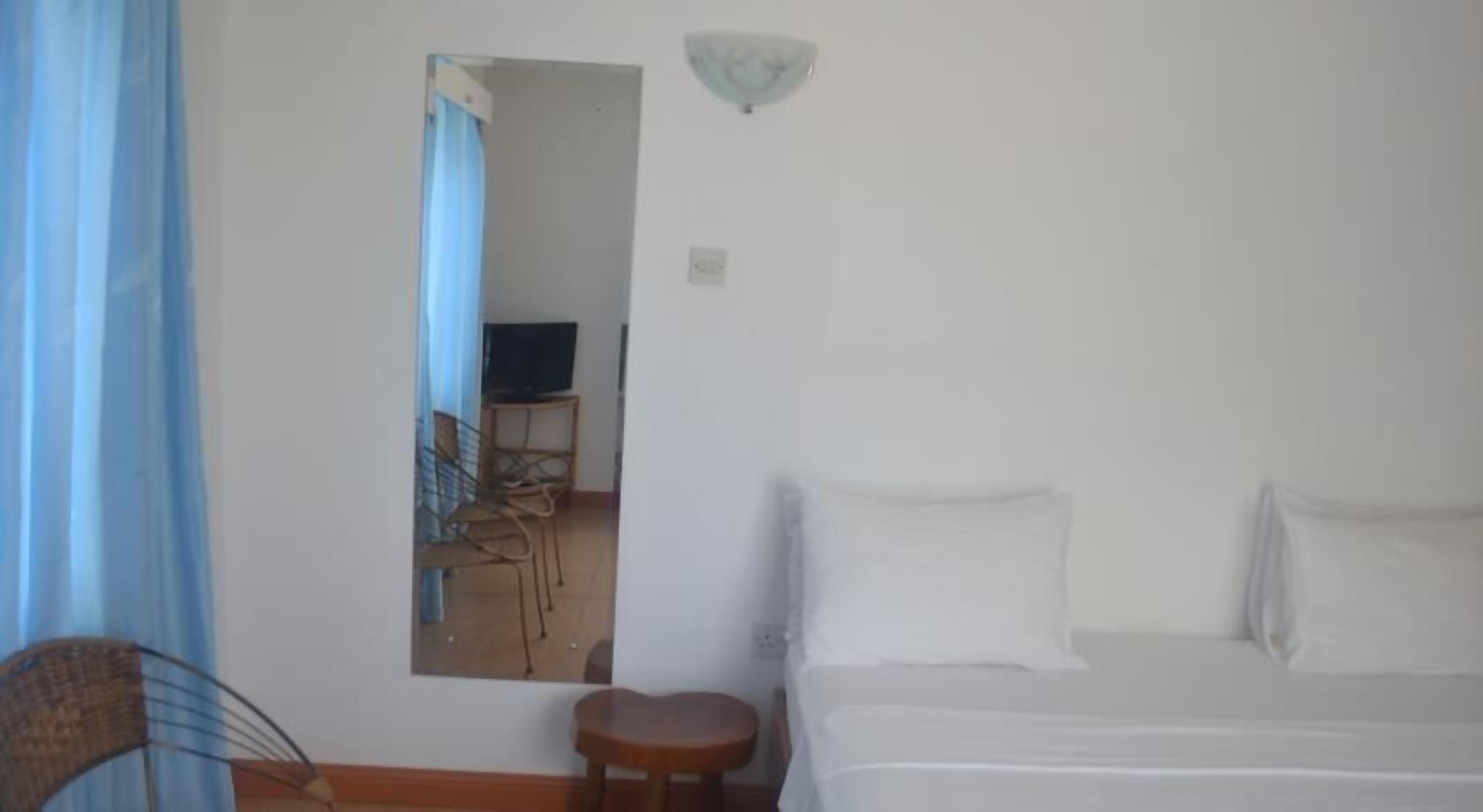 A hotel room with a bed, a small table, a chair, a TV, and a mirror.