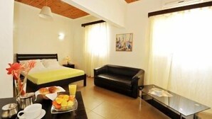 A hotel room with a bed, a sofa, a glass table, and a breakfast setup. - Cocoa Hotel Residence São Tomé (São Tomé)