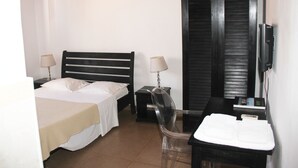 A hotel room with a bed, a chair, a desk, a TV, and a small table with towels. - Cocoa Hotel Residence São Tomé (São Tomé)