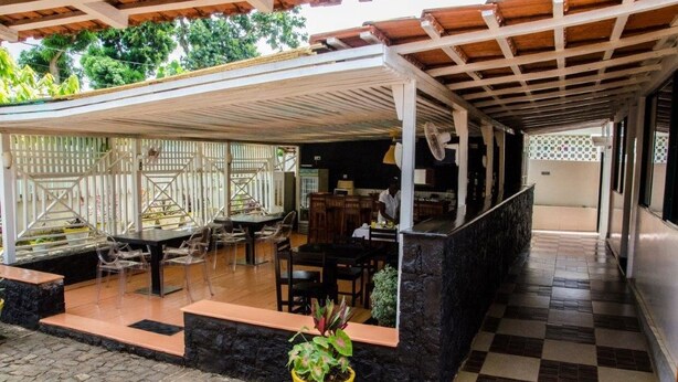 A covered outdoor area with a dining table and chairs, a potted plant, and a stone wall. - Cocoa Hotel Residence São Tomé (São Tomé)