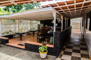 A covered outdoor area with a dining table and chairs, a potted plant, and a stone wall. - Cocoa Hotel Residence São Tomé (São Tomé)