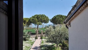 A garden pathway leading to a gazebo with a view of trees and a body of water.