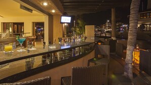 A bar area with a television, bar stools, and a city view at night. - Casa Diamond (Cabo San Lucas)