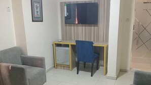 Een woonkamer met twee grijze banken, een kleine tafel, een blauwe stoel, een televisie en een lijst met een afbeelding aan de muur.