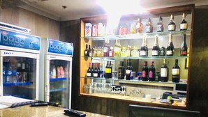 Een bar met een toonbank, een koelkast en planken vol diverse flessen.