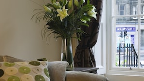A living room with a sofa, a vase with flowers, a newspaper, and a view of a building outside. - Haddington Place (Edinburgh)