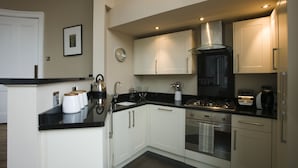 A modern kitchen with white cabinets, a black countertop, stainless steel appliances, and a clock on the wall. - Haddington Place (Edinburgh)