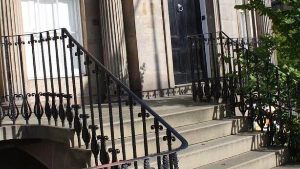 A building with classical architecture, featuring columns, a black door, and a staircase with ornate metal railings. - Haddington Place (Edinburgh)