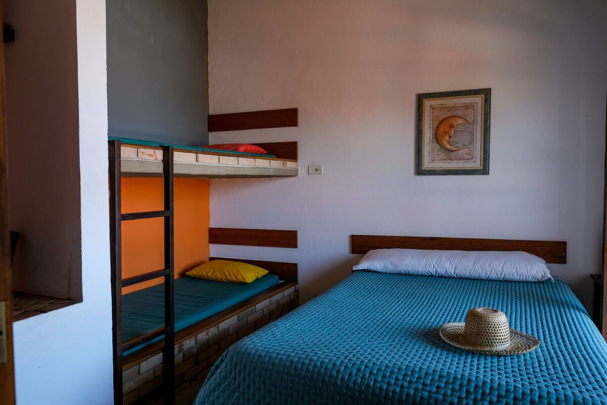 Una habitación con literas, una cama individual y un cuadro colgado en la pared.