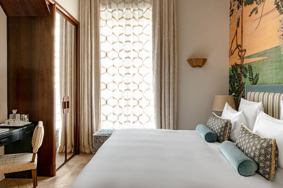 Una habitación de hotel con una cama grande, un escritorio con una silla y una ventana con cortina estampada.