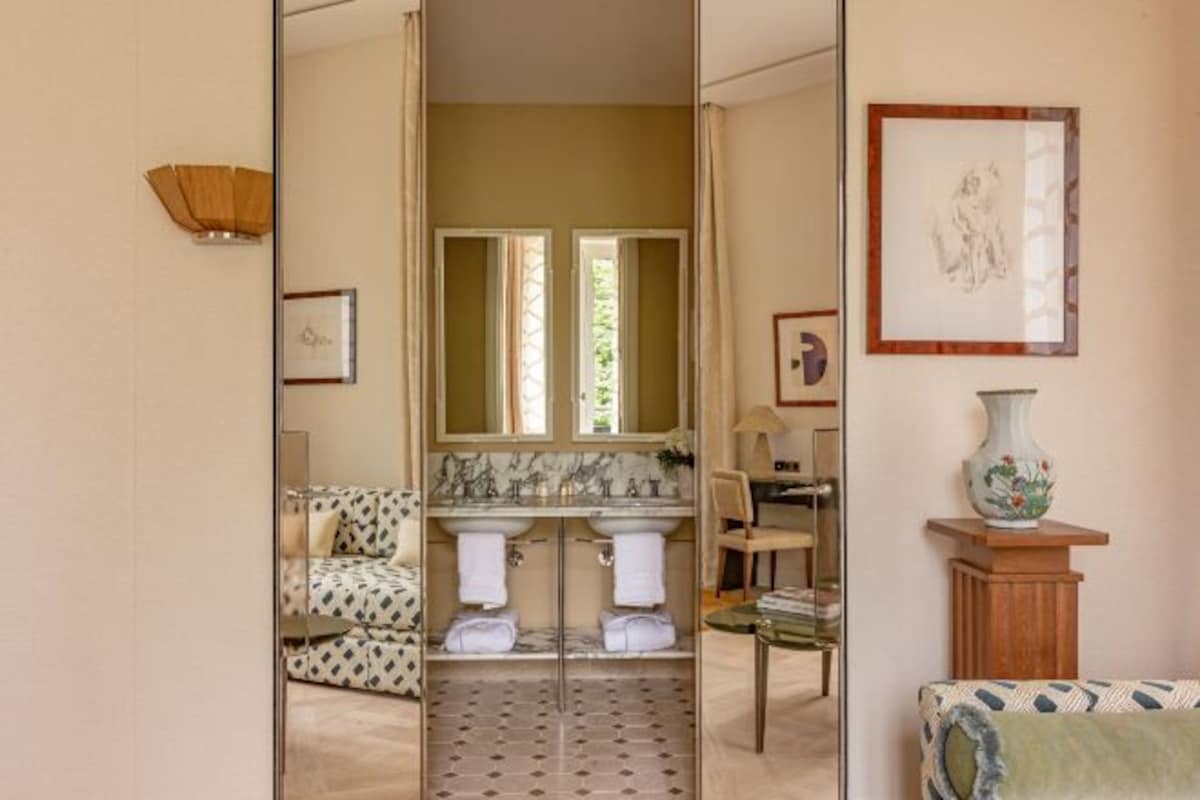 A bathroom with a large mirror, two sinks, a towel rack, and a framed picture on the wall.
