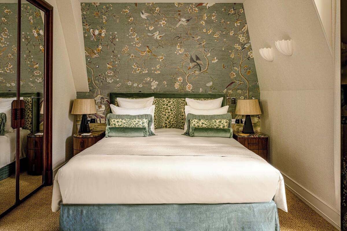 Habitación de hotel con una cama grande, dos mesitas de noche con lámparas, un espejo y un diseño de papel tapiz floral.