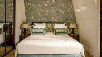 Quarto de hotel com uma cama grande, duas mesas de cabeceira com luminárias, um espelho e um papel de parede com padrão floral.
