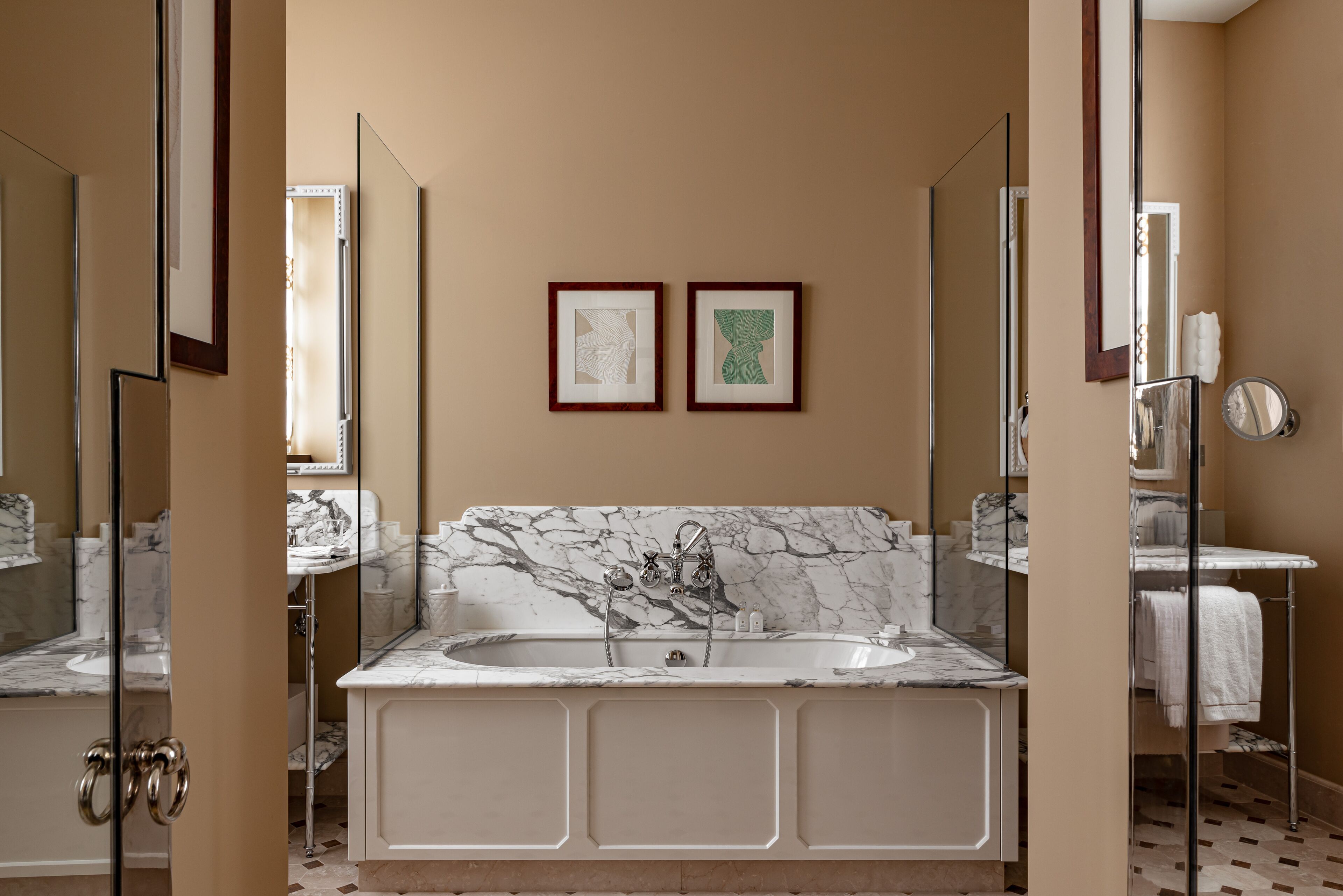 A bathroom with a marble sink, a bathtub, and two framed artworks on the wall.