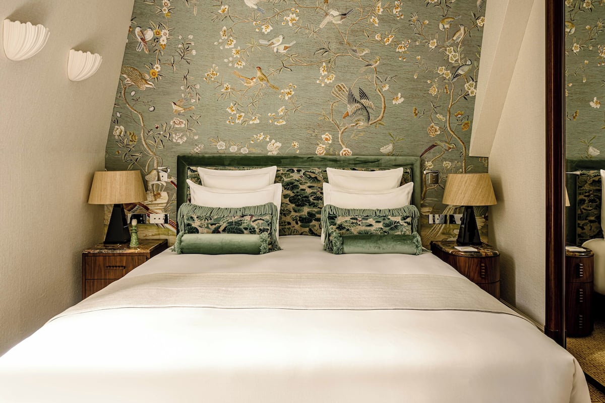 Una cama doble con dos almohadas, una mesita de noche con lámpara y un papel tapiz floral.