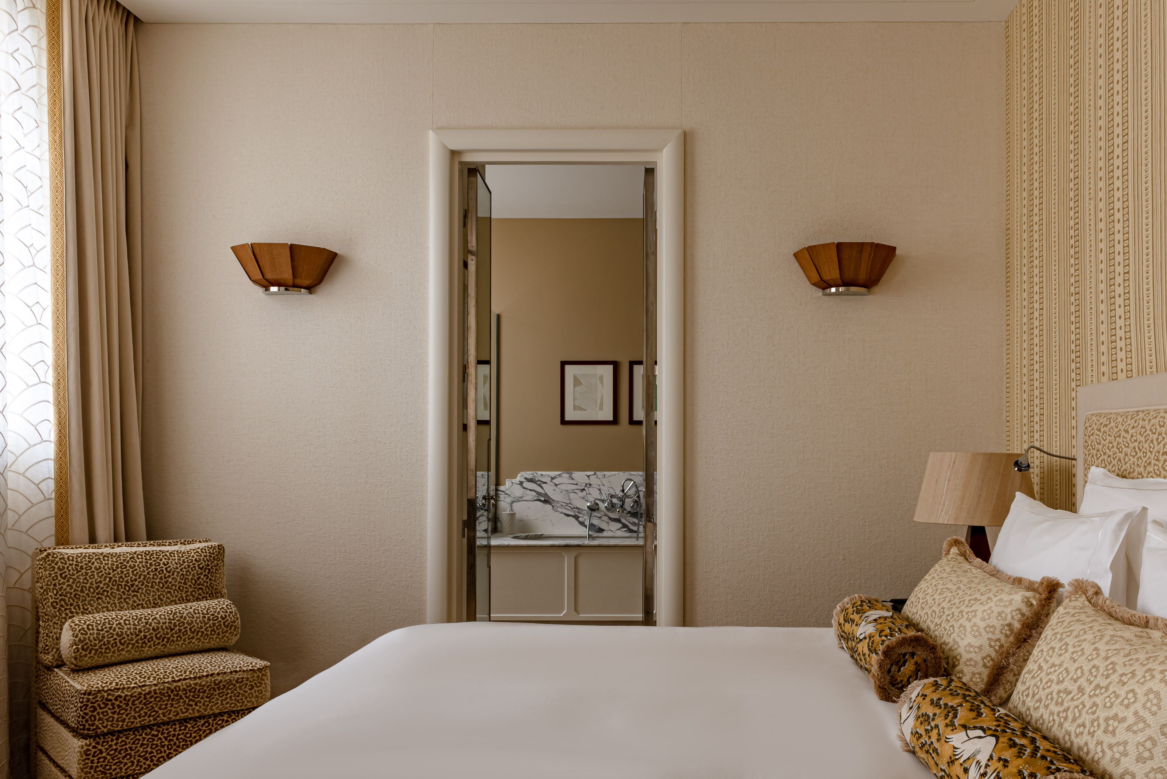 Een hotelkamer met een bed, een stoel, een badkamer met een marmeren wastafel en twee wandlampen.