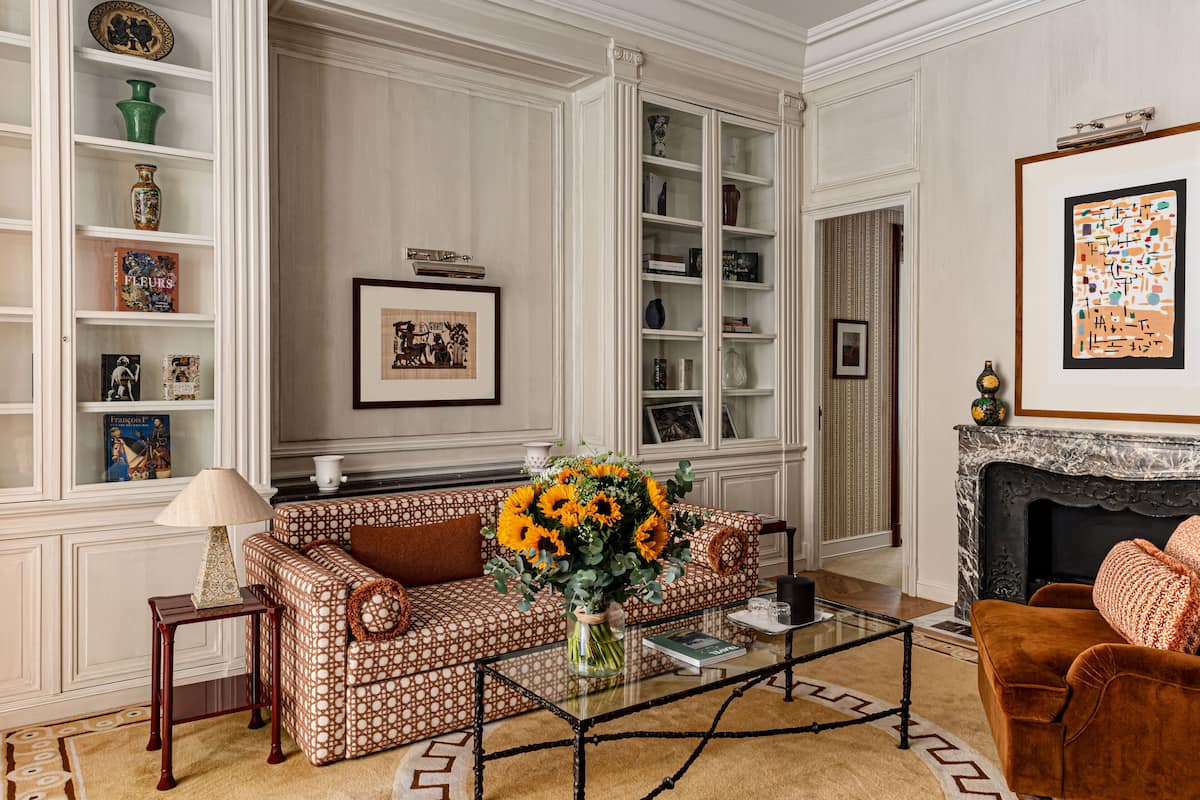 Una sala de estar con un sofá estampado, una mesa de centro, una chimenea y una estantería con objetos decorativos.