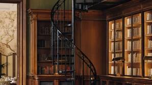 Una biblioteca con una escalera de caracol, sillones de cuero y una alfombra estampada.