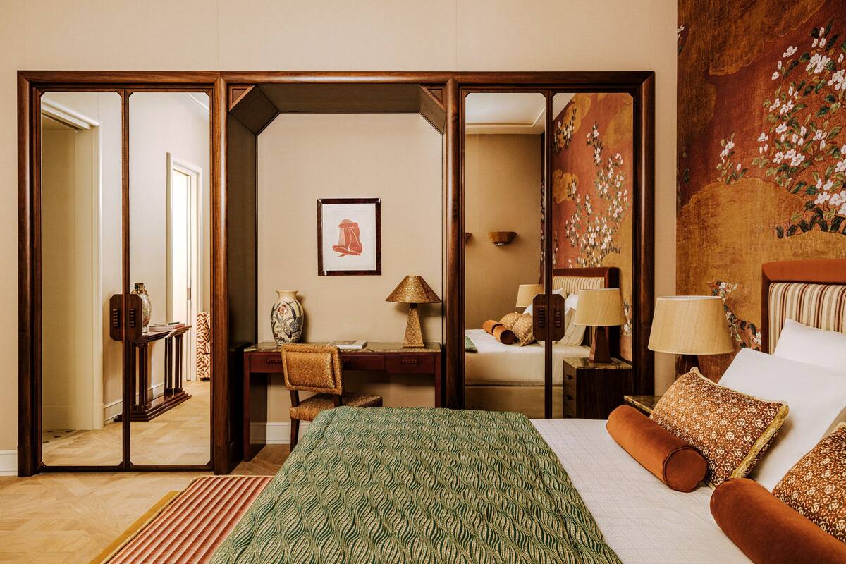 Habitación de hotel con cama, escritorio, silla, lámpara, un cuadro y un espejo.