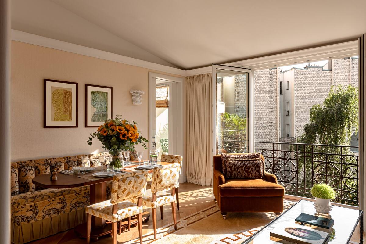 Una sala de estar moderna con sofá, mesa de comedor y sillas, un balcón con vista a un edificio de piedra y una planta en maceta sobre una mesa de centro.