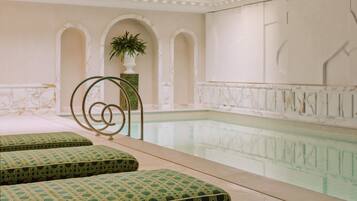 Un espace piscine doté d’un sol carrelé, d’une piscine à bords nets et de deux coins salon agrémentés de coussins verts.