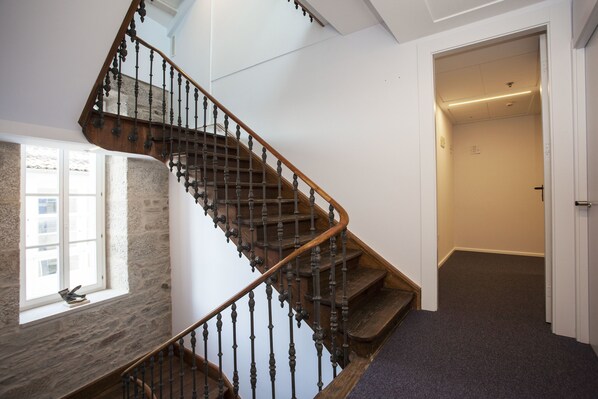 A spiral staircase with wooden balusters and steps, leading to a landing with a window overlooking a stone wall.