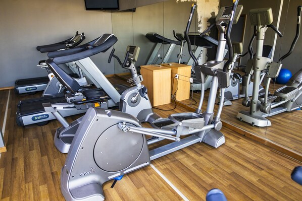 A gym with various exercise machines, including treadmills and stationary bikes, arranged on a wooden floor.