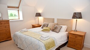 A bedroom with a bed, two nightstands, a dresser, and a window. - The Mill House (Earlston)