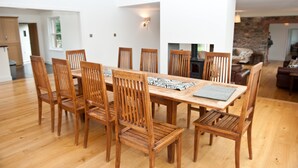 A spacious dining area with a long wooden table and matching chairs, a stone fireplace, and a view of the living room. - The Mill House (Earlston)