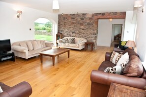 A living room with a stone wall, wooden flooring, and two sofas. - The Mill House (Earlston)