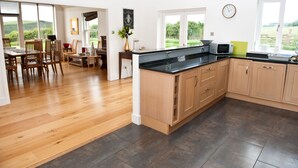 A spacious kitchen with wooden cabinets, a black countertop, and a dining area with wooden chairs and a table. - The Mill House (Earlston)