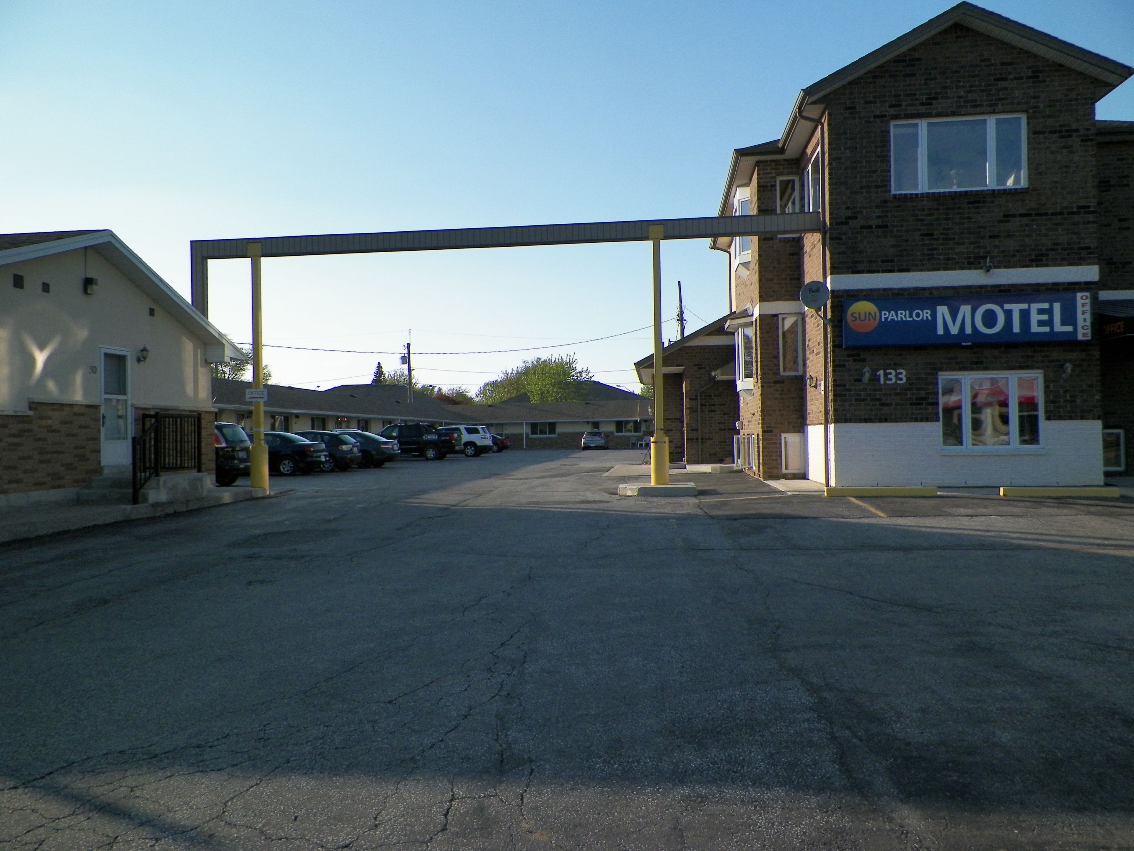 A motel with a parking lot, a building with a sign that reads "SUN PARLOR MOTEL", and a number "133" on the building.