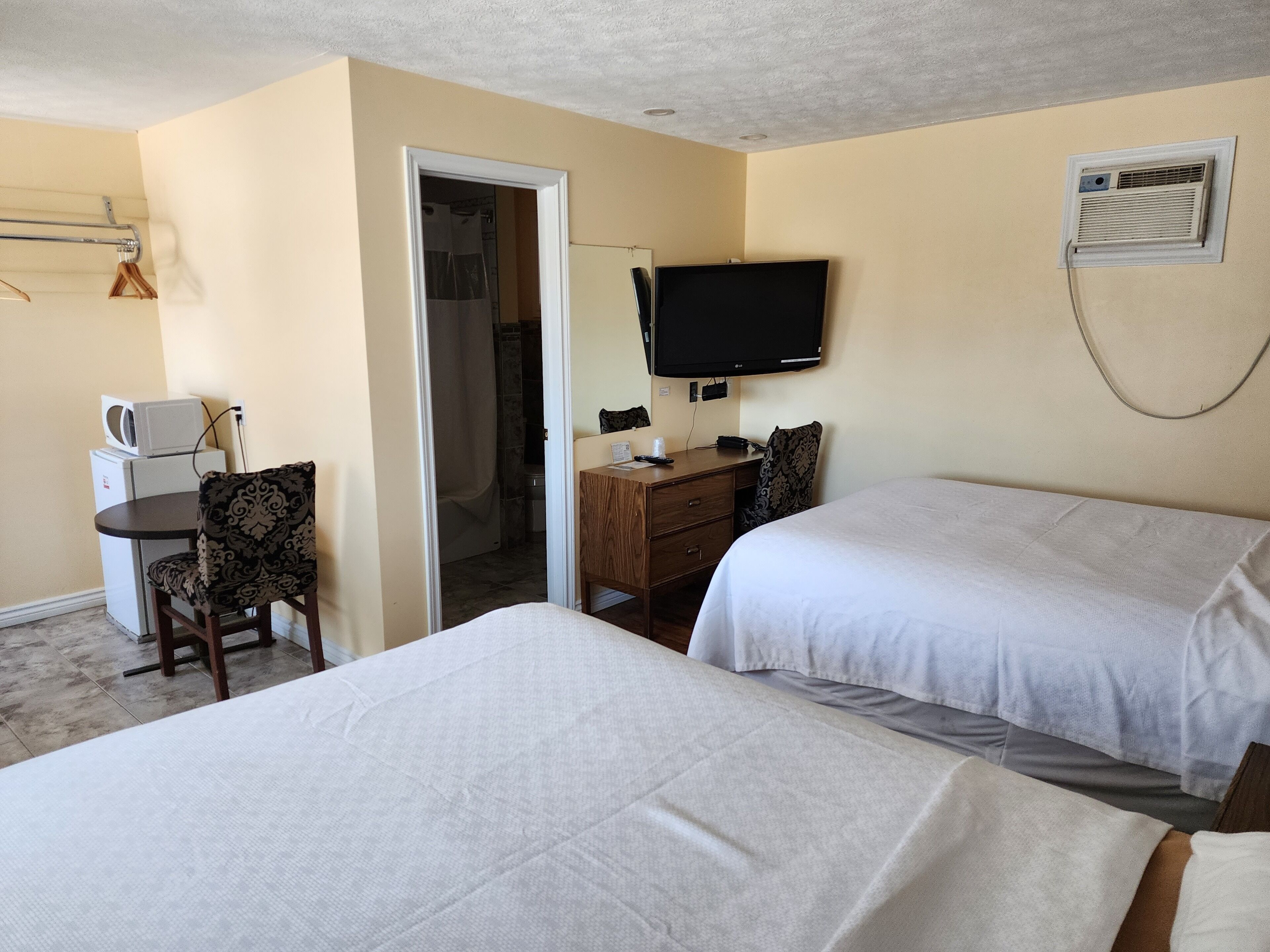 A hotel room with two beds, a desk with a chair, a television, and a microwave.