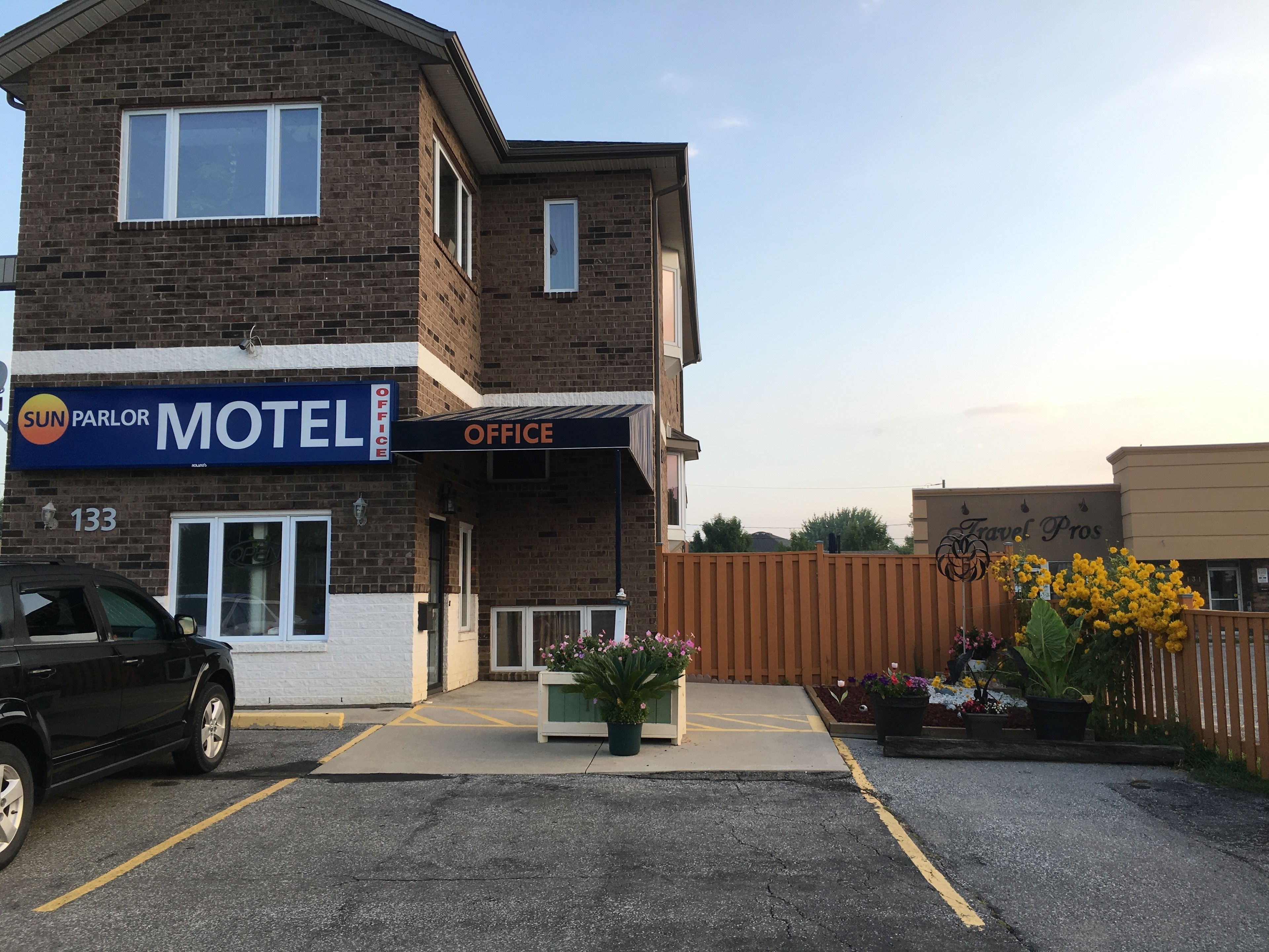 A motel with a 'Sun Parlor' sign, a 'Travel Pros' sign, and a parking lot with a black car.