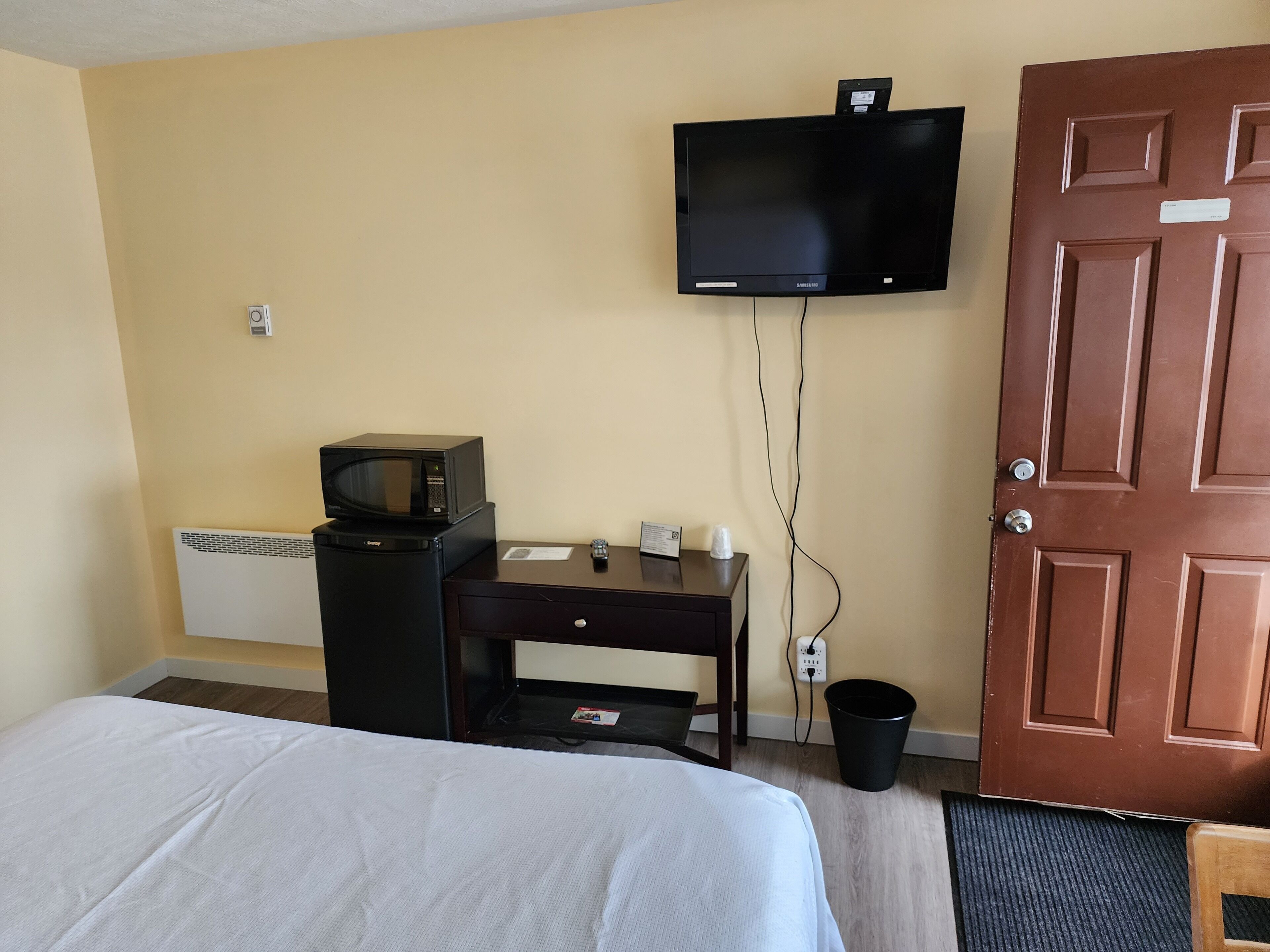 A hotel room with a bed, a desk with a microwave, a television, and a door.