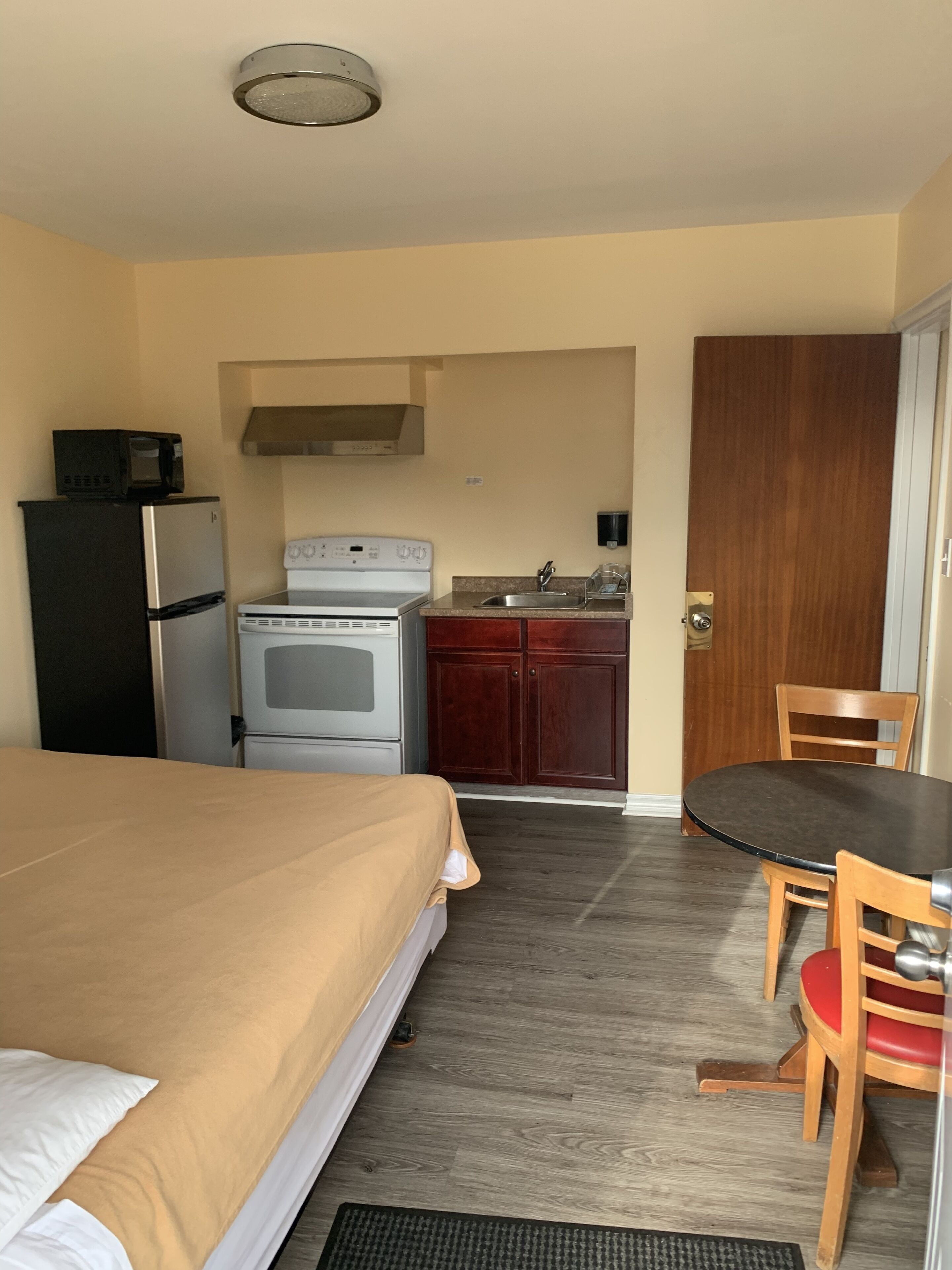 A hotel room with a bed, a small kitchenette, a dining table with chairs, and a wooden door.