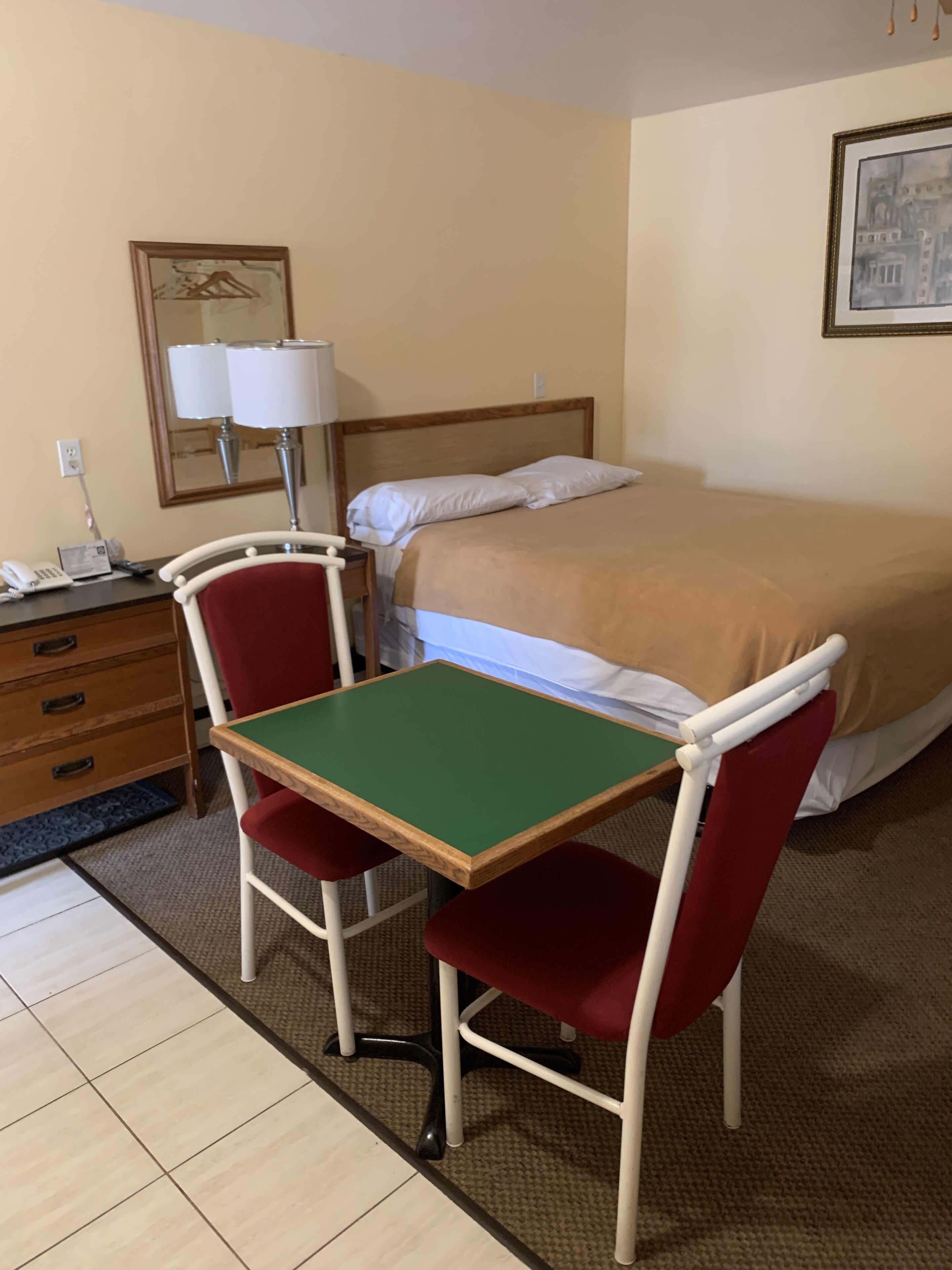 A hotel room with a bed, a desk with a chair, a lamp, and a dresser.