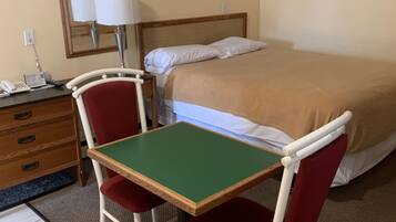 A hotel room with a bed, a desk with a chair, a lamp, and a dresser.