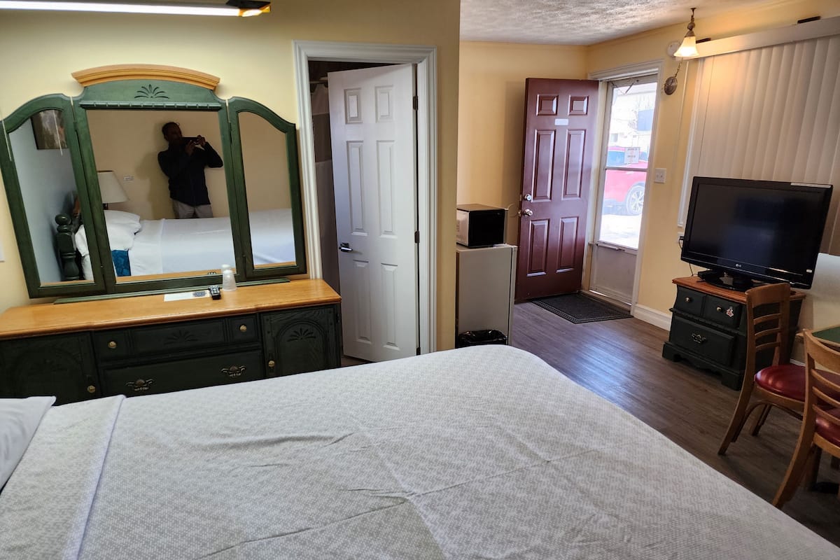 A hotel room with a bed, dresser, mirror, television, and a door leading to another room.