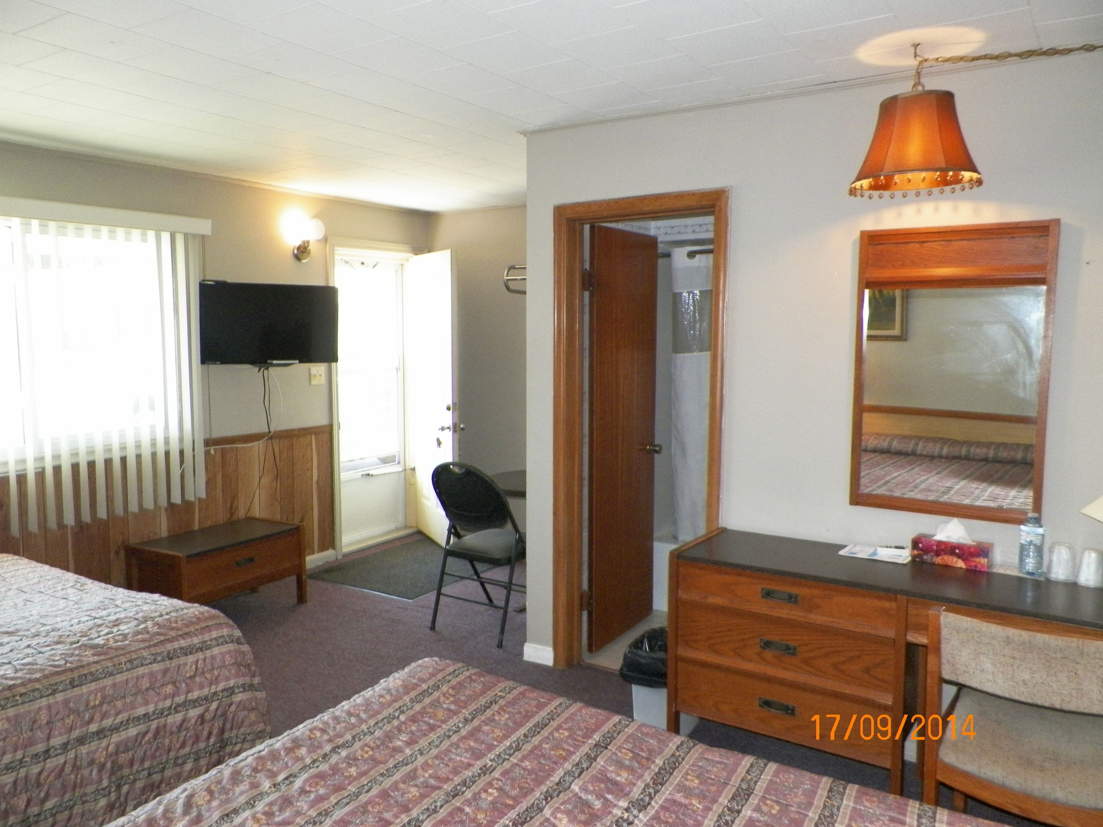 A hotel room with two beds, a desk, a chair, a television, and a mirror.