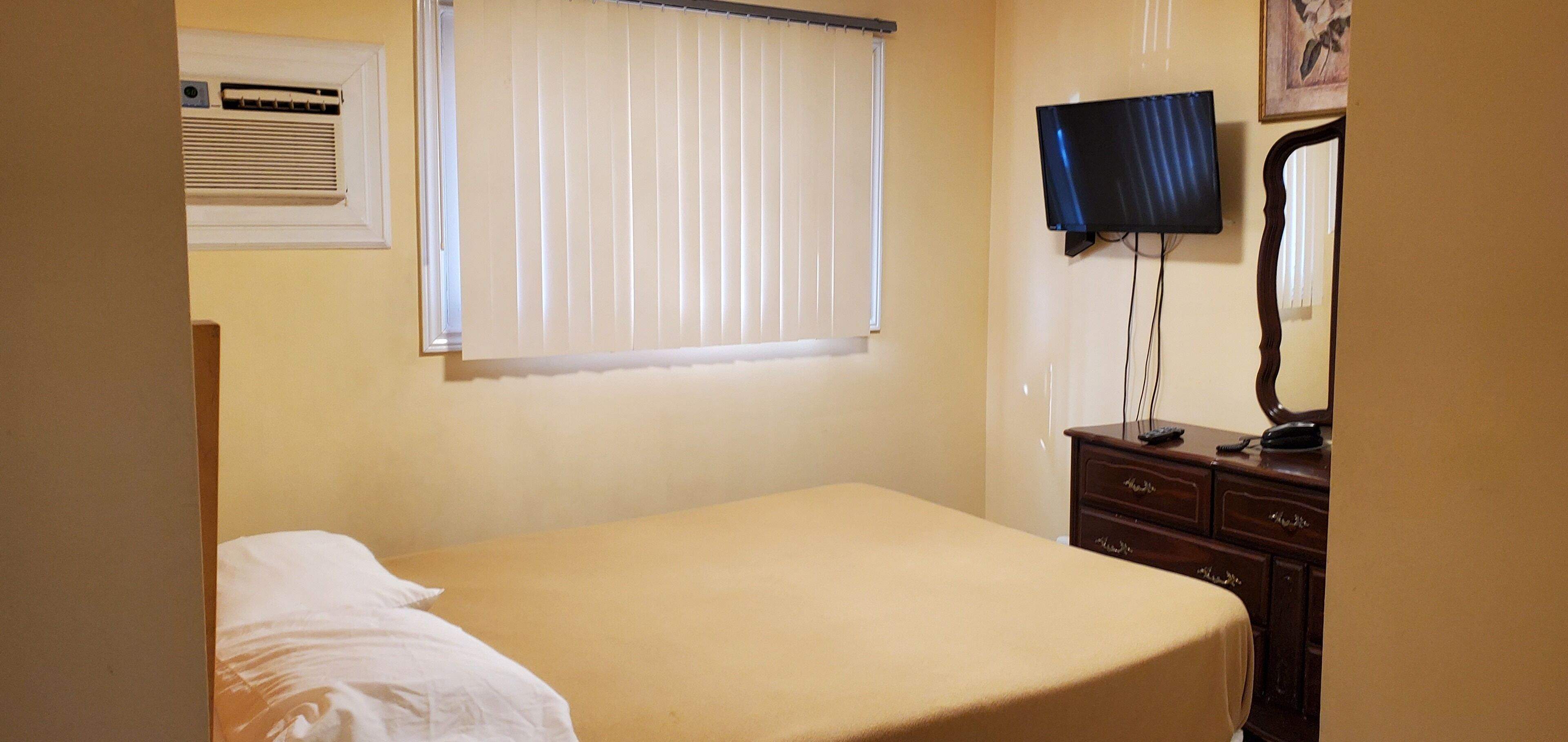 A bedroom with a bed, a dresser, a television, and a window with blinds.