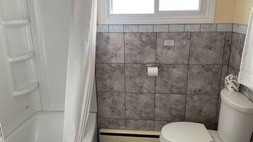 Et badeværelse med badekar, toilet og bruseforhæng.