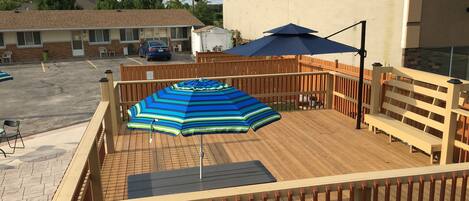 A wooden deck with a striped umbrella, a bench, and a table.