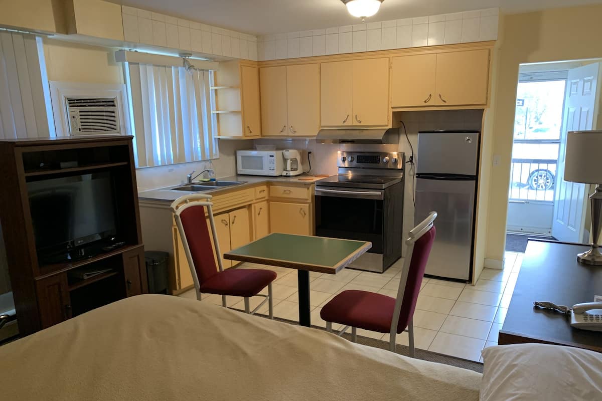 A compact kitchen with a microwave, stove, and refrigerator. There is a small dining area with two chairs and a table. A television is mounted on the wall.