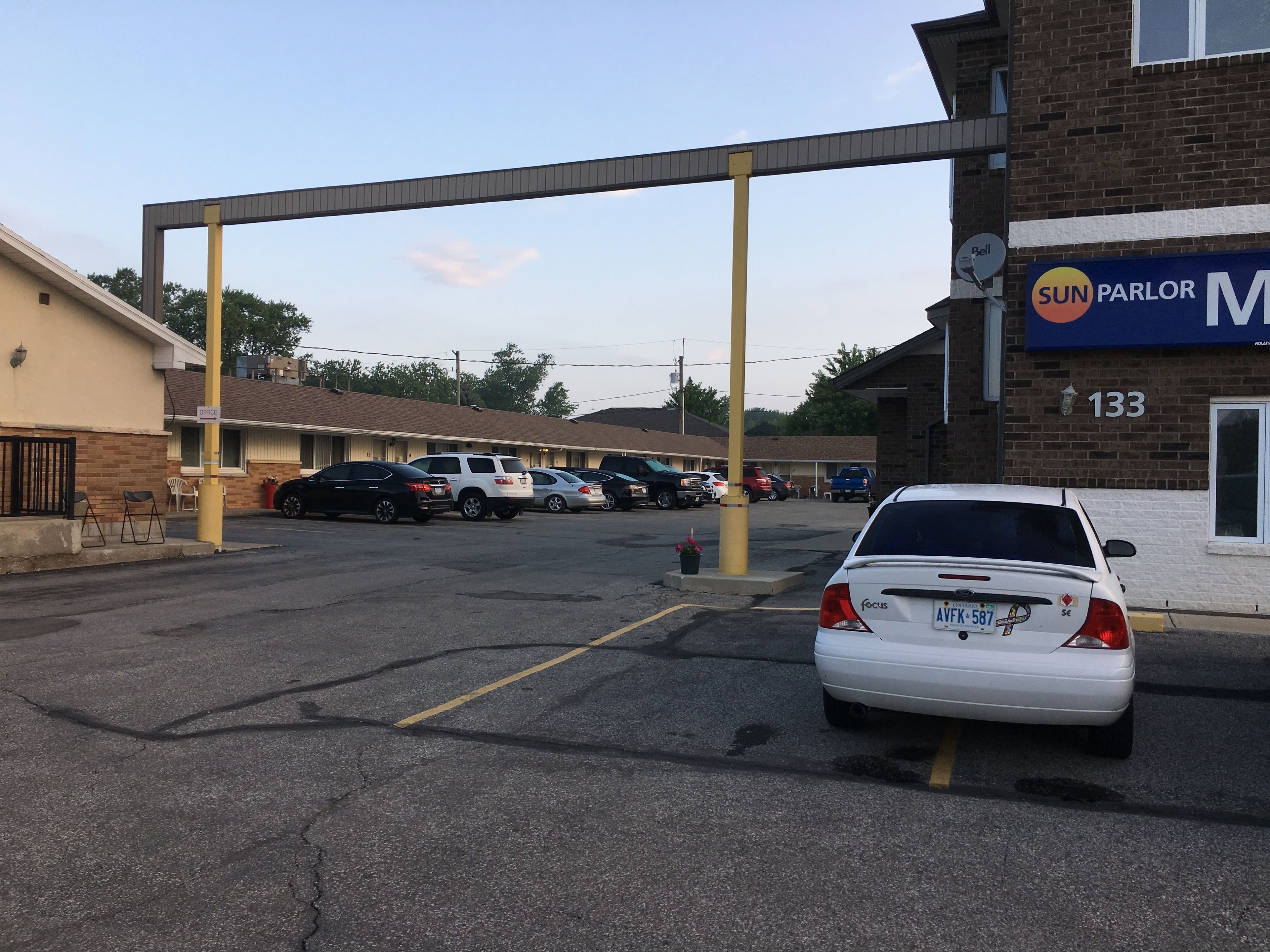 Un estacionamiento con varios coches, un edificio con un cartel que dice "SUN PARLOR" y el número "133" en la pared.
