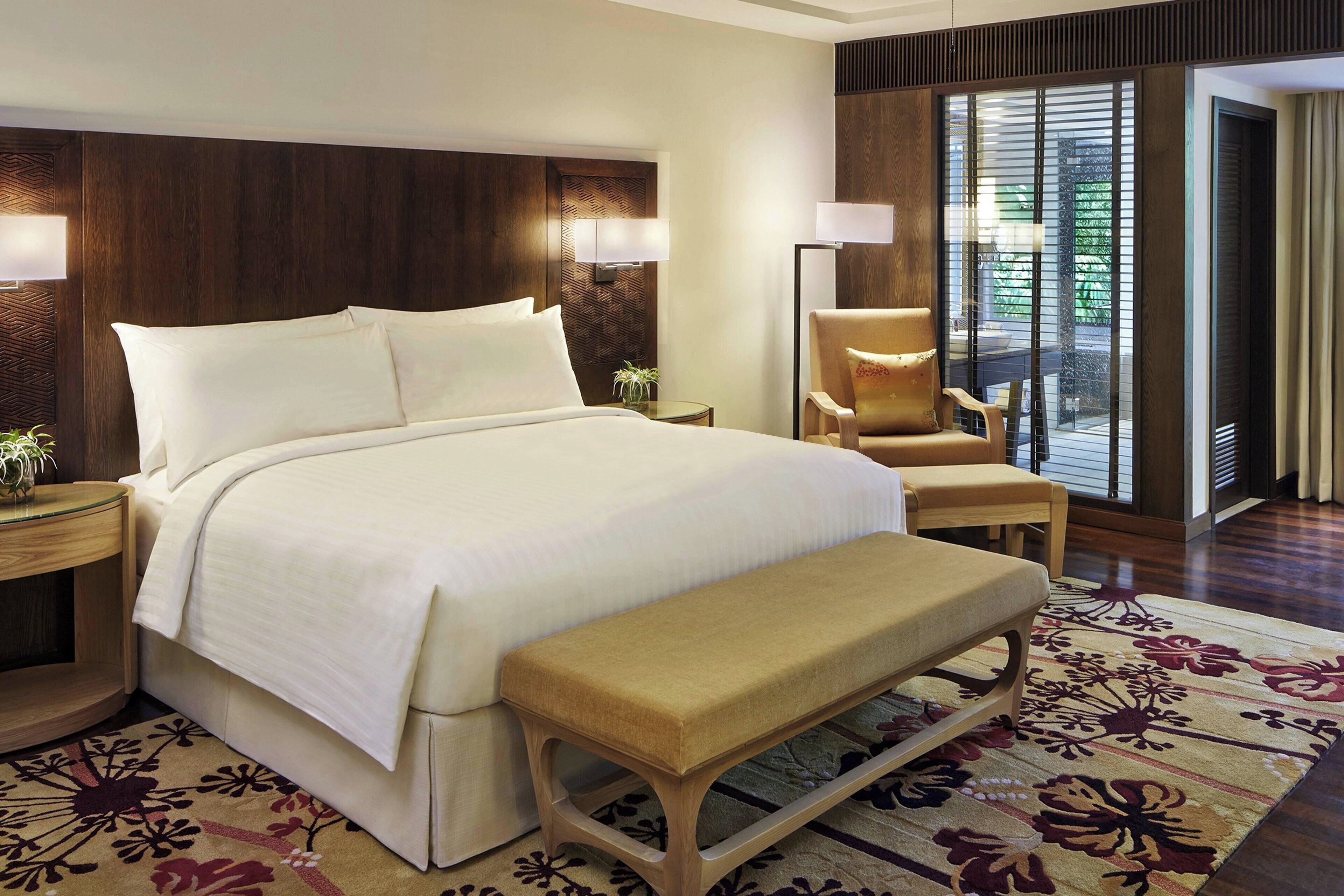 A hotel room with a large bed, a bench, a chair, a nightstand, and a floor lamp.