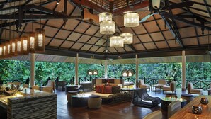 A spacious indoor area with a high ceiling, multiple hanging light fixtures, and a view of lush greenery outside. - Mulu Marriott Resort (Mulu)