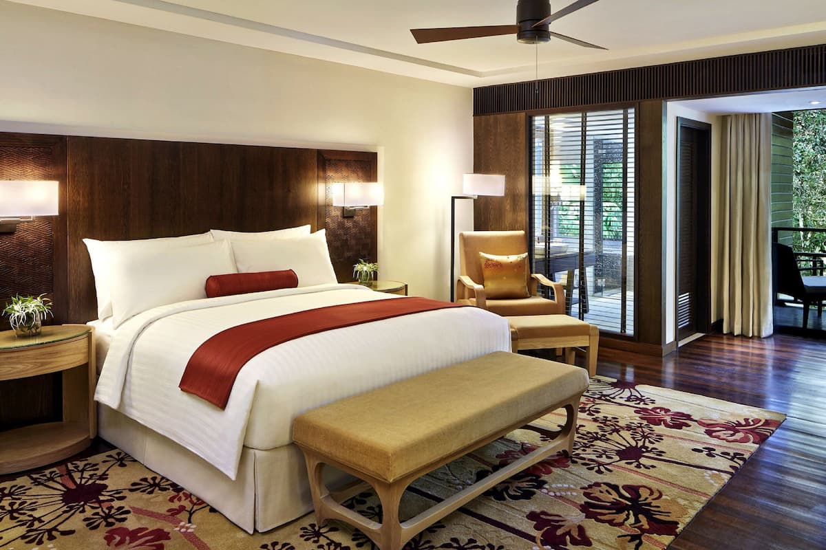 A hotel room with a large bed, a bench, a chair, a desk, and a view of the outdoors.