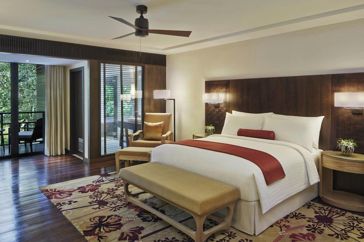 A hotel room with a bed, a bench, a chair, a nightstand, and a view of the outdoors.